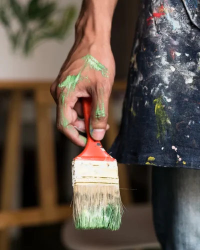Mano sujetando una brocha con restos de pintura verde durante un trabajo de pintura