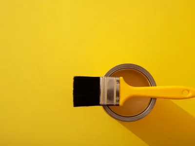 Brocha apoyada sobre bote de pintura amarilla sobre fondo amarillo