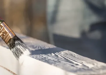 Brocha aplicando pintura blanca sobre superficie en trabajo de acabado